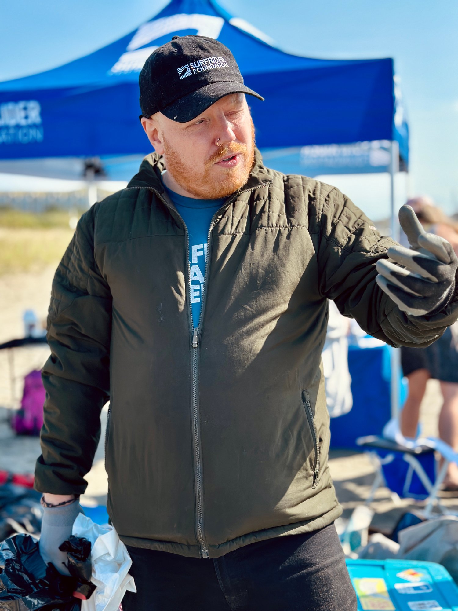 A male volunteer wearing a Surfrider hat giving a speech during a beach cleanup 