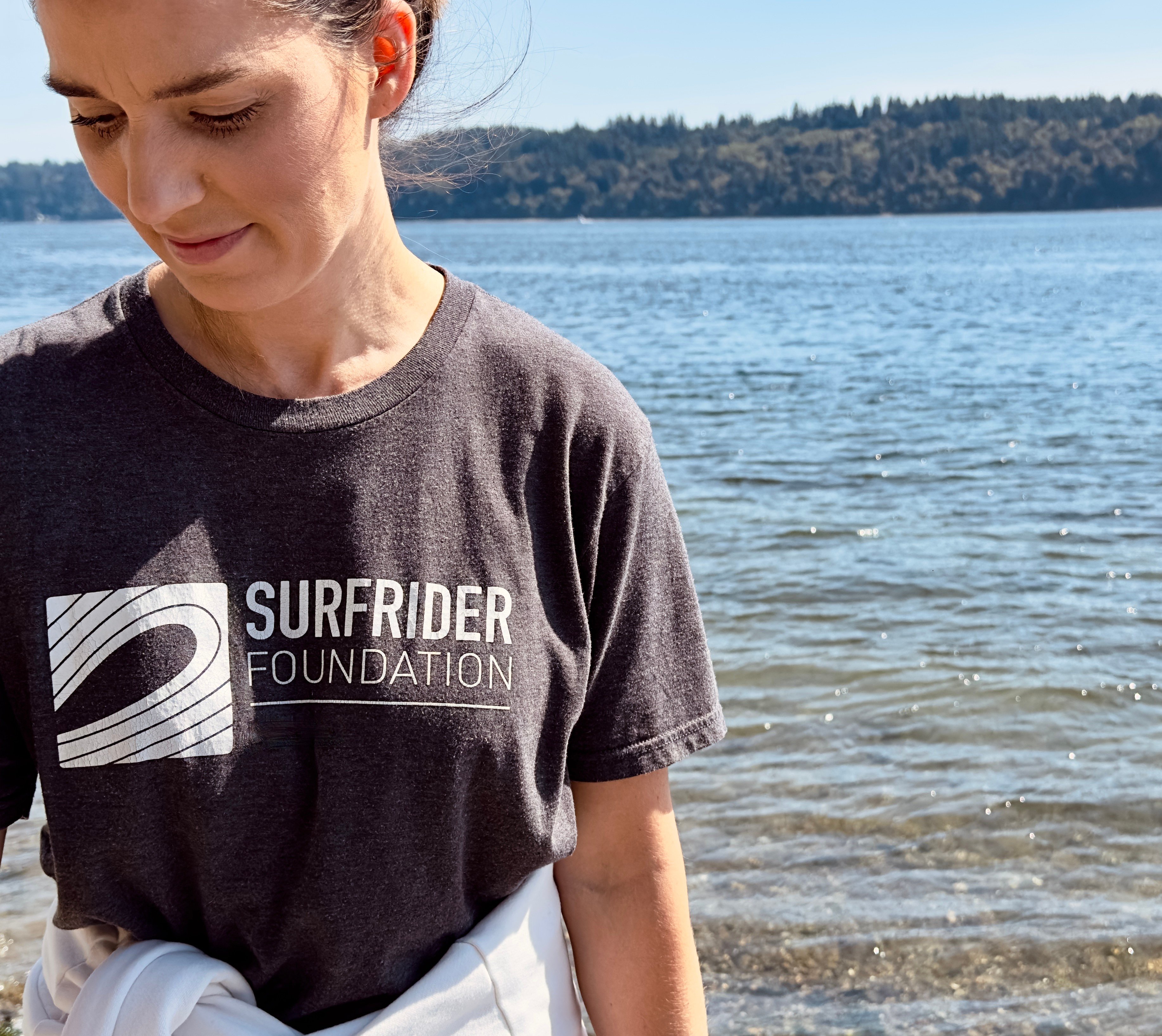 Female volunteer standing at the coastline of the Puget Sound wearing a Surfrider Foundation t-shirt